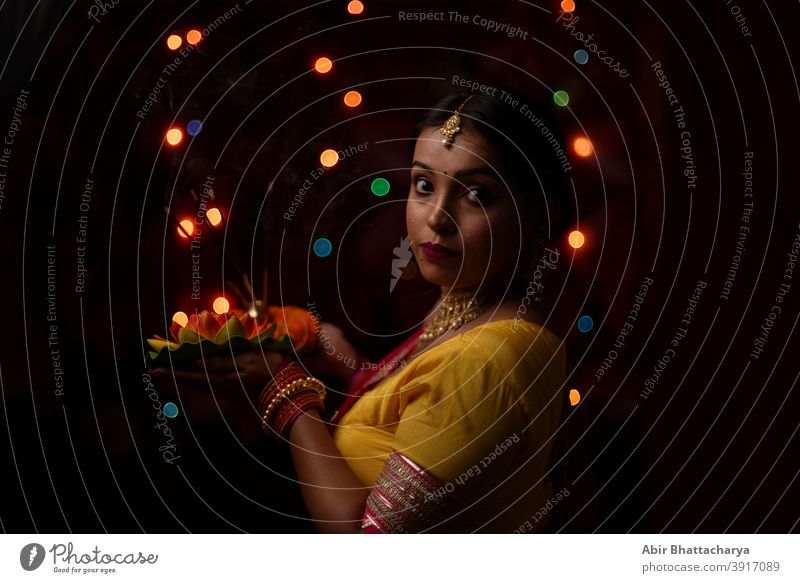 Eine junge und schöne indisch-bengalische Frau in indischer Tracht hält vor bunten Bokehlichtern eine Diwali diya/Lampe in der Hand. Indischer Lebensstil und Diwali-Feier