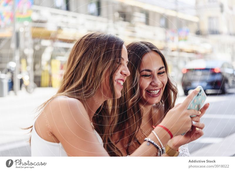 Lachende Freundinnen mit Smartphone auf der Straße Spaß haben Zusammensein benutzend zuschauen urban heiter Telefon jung Frau Mobile Sitzung Apparatur Gerät