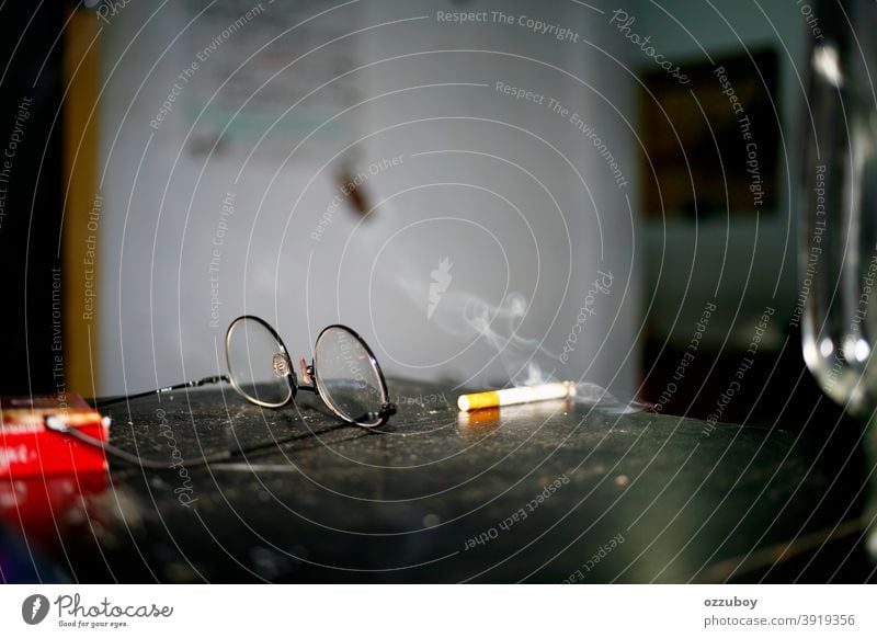 Zigarette und Brille auf dem Tisch Rauchen Sucht Tabak Tabakwaren Nikotin ungesund Unselbständigkeit gesundheitsschädlich Zigarettenrauch Nikotingeruch