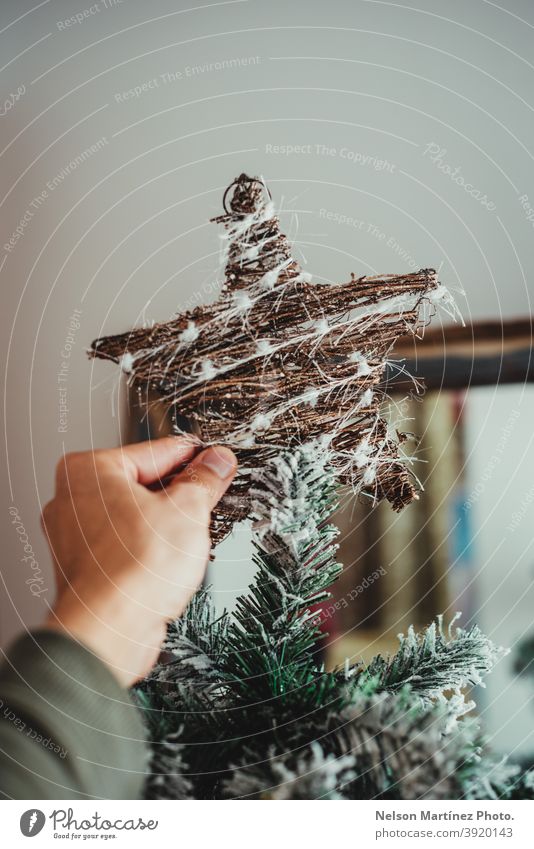 Nahaufnahme der Hand eines Mannes, der den Weihnachtsstern an den Baum hängt. Weihnachtsschmuck Weihnachtsdekoration erhängen verziert elegant vereinzelt