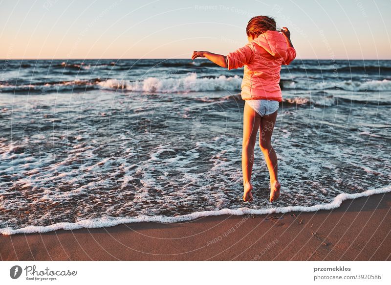 Verspieltes kleines Mädchen, das bei Sonnenuntergang am Sandstrand über die Meereswellen springt aufgeregt frei genießen positiv Emotion sorgenfrei Natur