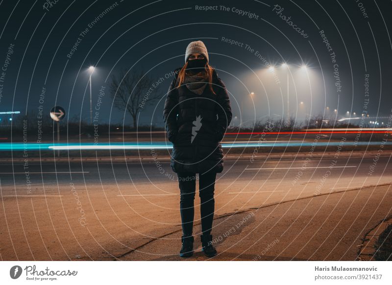 Frau mit Maske und Winterkleidung auf der Straße stehend, während Auto Lichter hinter vorbei, Zeit bewegen Konzept aktiv Aktivität Erwachsener Hintergrund schön