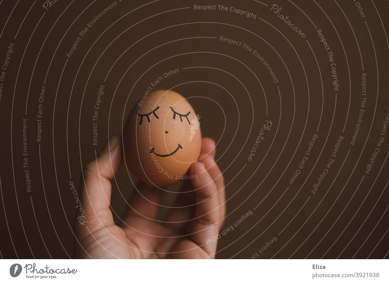 Hand hält ein Ei mit gemaltem Gesicht darauf. Ostern. bio glücklich Hühnerei Osterei lächelnd bioei Lebensmittel bemalt