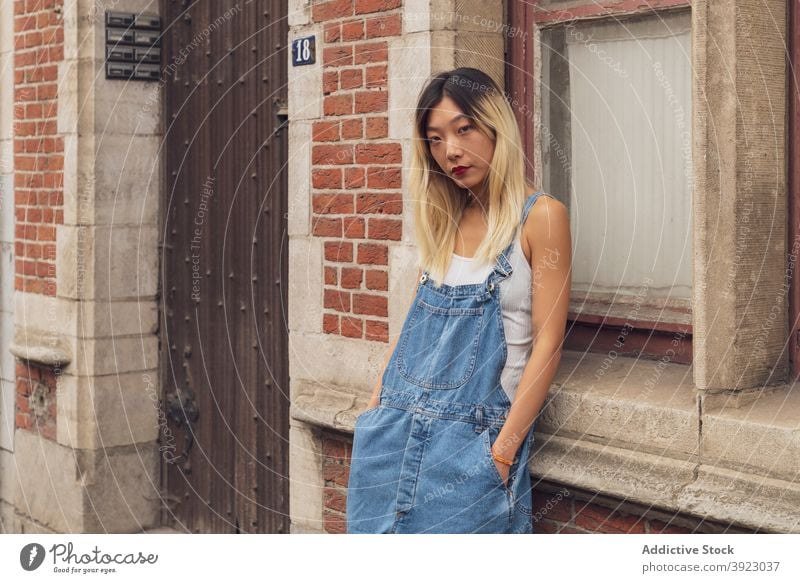 Stilvolle ethnische Frau steht auf der Straße Jeansstoff gesamt Großstadt trendy selbstbewusst Bekleidung Sommer urban asiatisch Gebäude Persönlichkeit modern