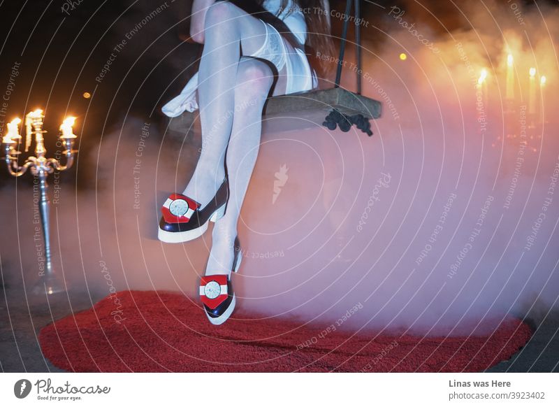 Modisches Mädchen mit avantgardistischen Schuhen schwingt unter der Brücke. Rauch mit Kronleuchtern schafft eine mystische Atmosphäre. Dies ist kein typisches Mode-Fotoshooting.
