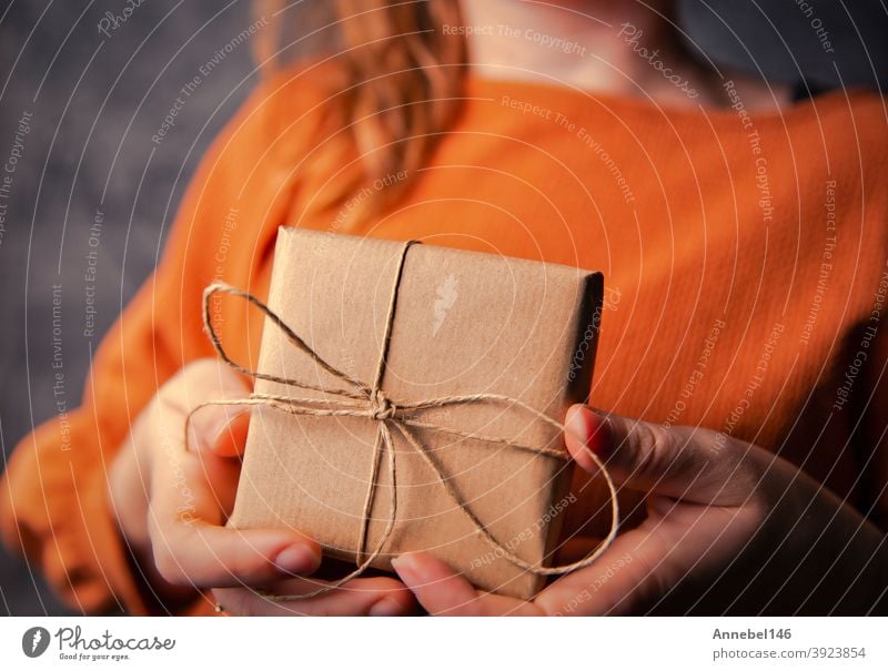 Junge Frau hält eine Kraft-Geschenk-Box, eingewickelt in einfachen braunen Papier, Valentinstag, Geburtstag, Mothers Day Geschenk oder Geschenk-Konzept selektiven Fokus, dunklen Hintergrund