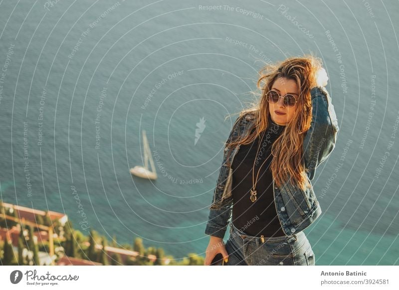 Porträt einer attraktiven Brünette mit Sonnenbrille posiert sinnlich mit dem hellblauen adriatischen Meer hinter ihr. Kleines Segelboot auf dem Meer in der Nähe von Dubrovnik, Konzepte der Reise mit copyspace Raum