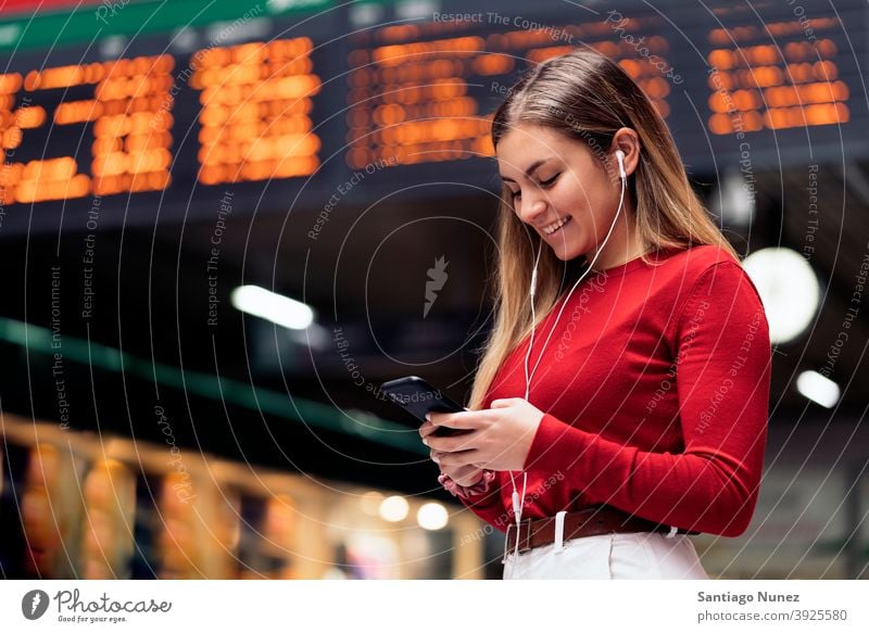 Mädchen im Bahnhof Station Seitenansicht Blick auf das Telefon Kopfhörer Porträt jung 20s blond hübsch per Telefon Funktelefon Kaukasier Stehen Frau Smartphone