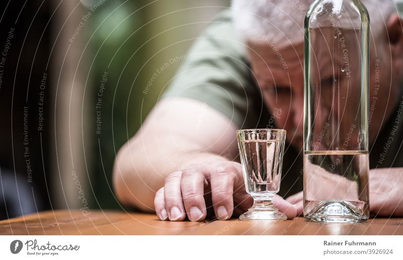 Ein Mann starrt auf sein volles Schnapsglas, daneben steht eine Flasche mit Alkohol Alkoholiker Wodka Glas trinken Getränk Alkoholsucht Farbfoto Spirituosen