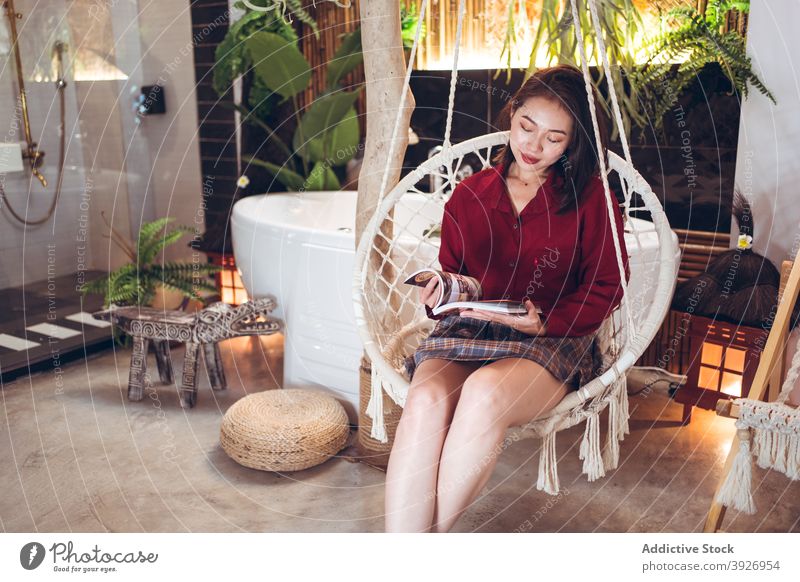 Ethnische Frau mit Zeitschrift entspannt im Stuhl lesen Magazin sich[Akk] entspannen ruhen Hotel Kälte Reisender gemütlich Seil hängen jung asiatisch ethnisch