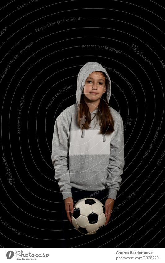 Kleines Mädchen in grauem Sweatshirt und zwei Zöpfen spielen mit einem Fußball isoliert auf schwarzem Hintergrund Sport Auge vereinzelt geschnitten Lifestyle