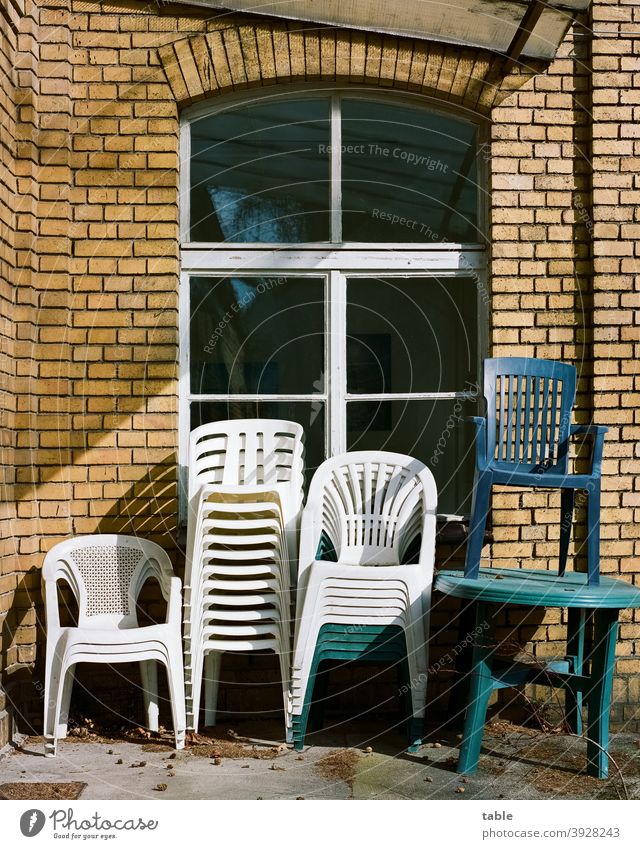 mehrere Stapelstühle aus Kunststoff stehen übereinandergestapelt an einer Hauswand Stuhl Sonnenlicht Außenaufnahme Farbfoto Ordnung Erholung ruhig geduldig