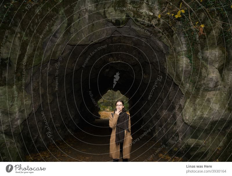 Es ist Herbst in Gent, Belgien. Das brünette Mädchen ist in einen modischen braunen Mantel gekleidet und ein langer schwarzer Schal ist ein Muss bei diesem furchtbaren Wetter. Sie raucht eine Zigarette neben einer Höhle.