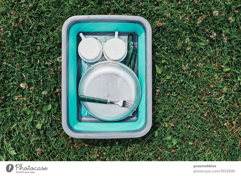 Abwaschschüssel gefüllt mit dem gewaschenen Außengeschirr, Teller, Tassen und Besteck auf den Rasen stellen Lager Camping Campingplatz Reinigen Säuberung Speise