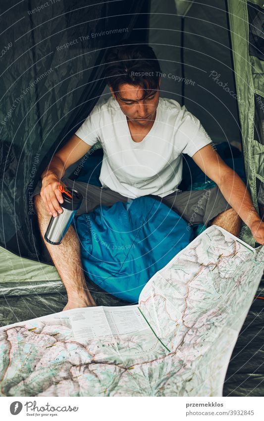Junger Mann schaut auf eine Karte der Bergwege Planung der nächsten Reise auf Sommerurlaub sitzen in einem Zelt auf Camping Untersuchen Landkarte Tourist reisen