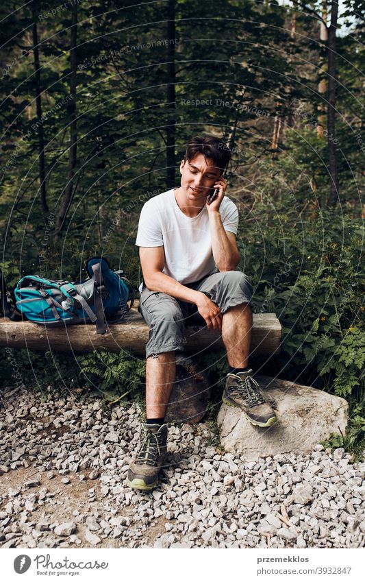 Junger Mann mit Rucksack sprechen am Telefon mit Pause sitzen auf Stamm während der Wanderung in einem Gebirge Aktivität Abenteuer Wald Waldlandschaft Schneise