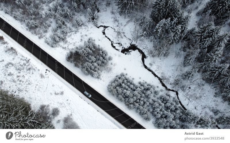 Luftaufnahme mit einer Drohne von einer Straße mit einem Auto das im Winter durch den Wald fährt luftaufnahme drohnenfoto auto winter straße fahren schnee wald