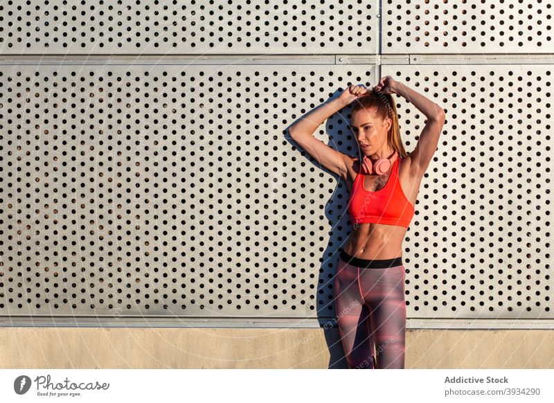 Sportlerin steht in der Nähe von Gebäude auf der Straße Läufer Großstadt Athlet schlank passen Sommer sonnig Frau stehen Sportbekleidung Wand Training