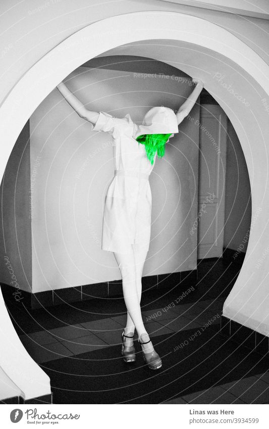 Grüne Haare - egal. Auch wenn das ganze Bild schwarz-weiß ist. Latex-Mode-Fotoshooting mit einem weiblichen Model mit enorm langen Beinen in High Heels und einem weißen Regenmantel mit Kapuzenpulli.