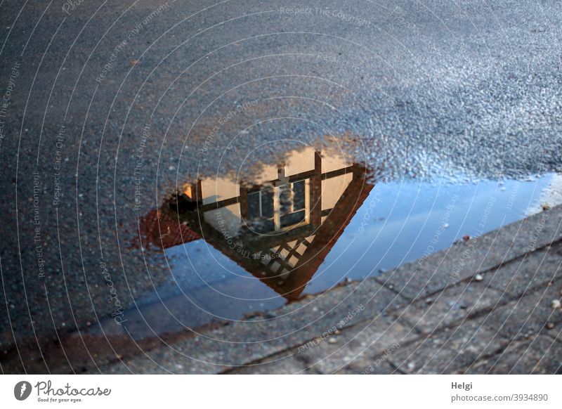 Giebel eines Fachwerkhauses als Spiegelung in einer Pfütze am Straßenrand Haus Gebäude Architektur Wasser nass Gehweg Asphalt Pflastersteine schönes Wetter