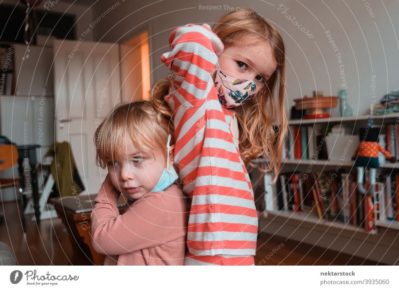 Geschwister Schwestern posieren Rücken an Rücken Stoffmaske Kind Mundschutz Kinder Frau Mädchen im Innenbereich heimwärts zu Hause Kaukasier Gesichtsmaske