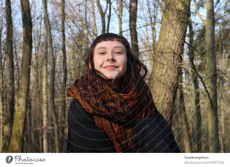 Porträt einer jungen lächelnden Frau mit Nasenpiercing unter kahlen Bäumen Junge Frau Frauengesicht verschmitzt weiblich junge Erwachsene brünett ponyfrisur