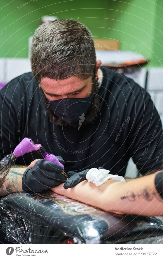 Fokussierter Meister beim Tätowieren auf dem Arm eines Kunden Mann Tätowierer Arbeit kreieren Konzentration Tattoo Tusche Instrument Maschine Klient Salon
