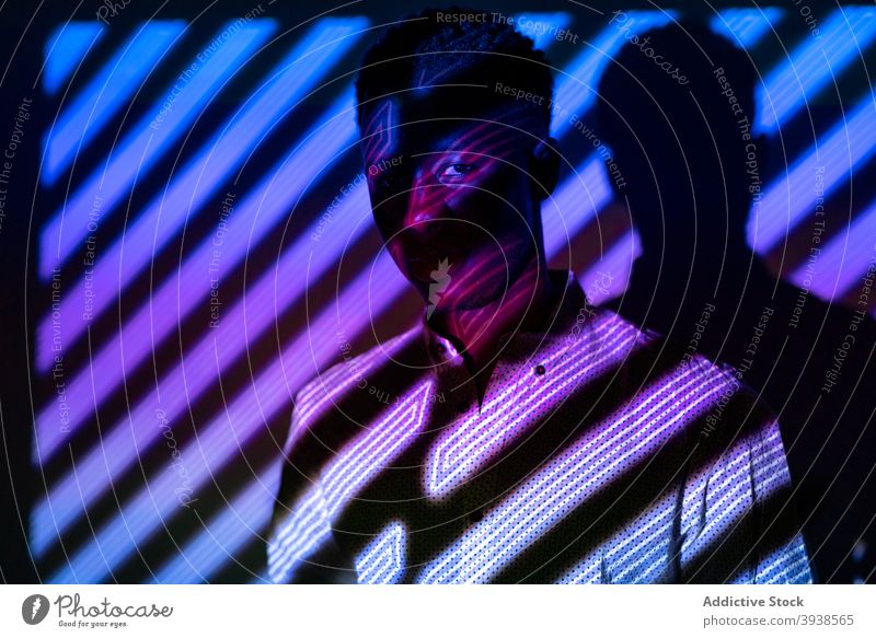 Schwarzer Mann in Neonlicht im Studio neonfarbig Licht leuchten Atelier Streifen Form Farbe trendy Mode männlich schwarz ethnisch Afroamerikaner dunkel Stil