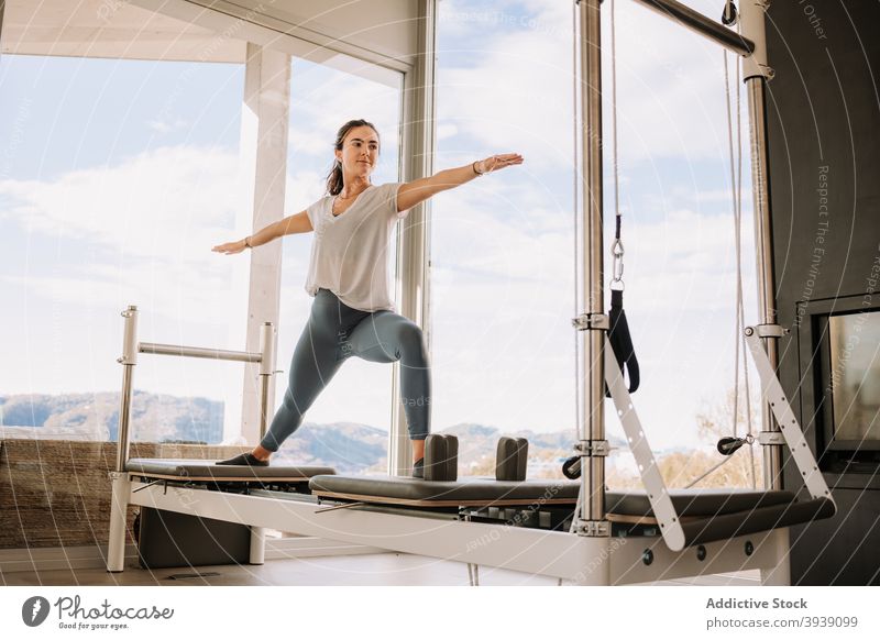 Frau macht Yoga auf Pilates Reformer üben Asana Krieger-Pose virabhadrasana Fitnessstudio beweglich Gesundheit Wellness passen Sportbekleidung Aktivität