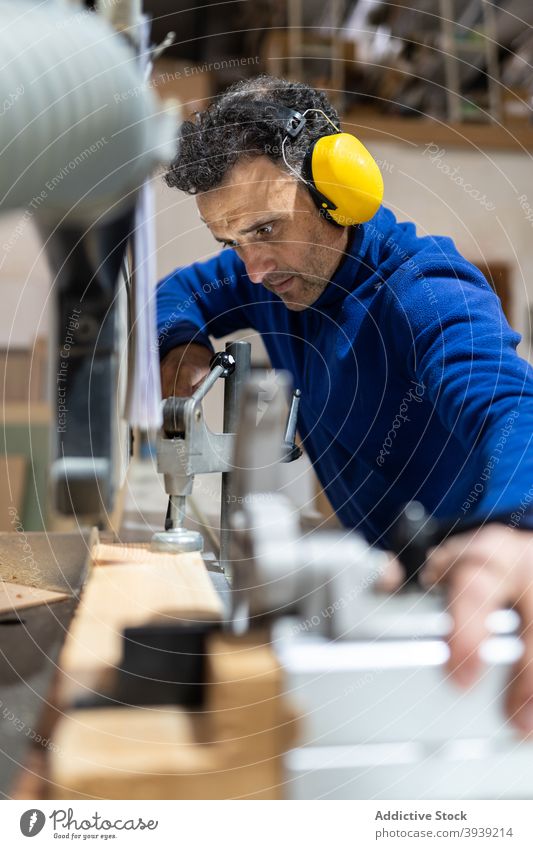 Professioneller Tischler beim Sägen eines Holzbretts in der Werkstatt Mann Maschine Job Zimmerer Tischlerarbeit Holzarbeiten Hobelbank Konzentration Beruf