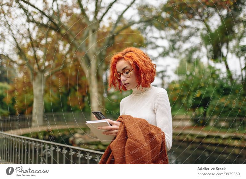 Friedliche rothaarige Frau, die im Park auf ihrem Smartphone surft Browsen Rotschopf Vorschein App Talkrunde soziale Netzwerke Internet rote Haare Surfen online