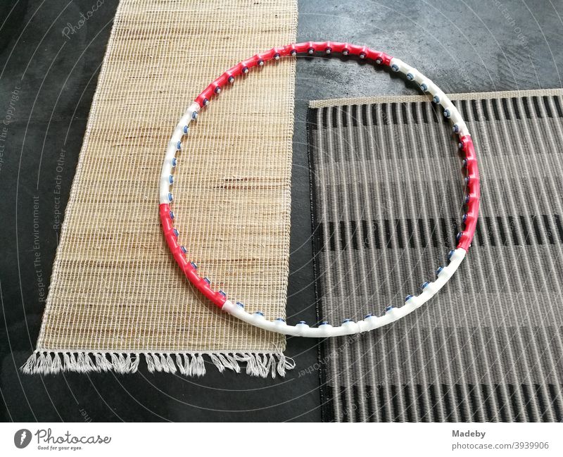 Hula Hoop Reifen in Rot und Weiß auf zwei schlichten modernen Teppichen aus Naturfaser auf dem grauem Betonboden einer Designerwohnung Fitness Sport Gymnastik