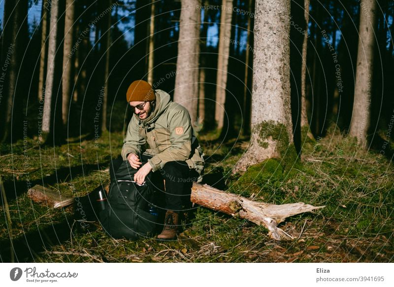 Ein Mann sitzt im Wald auf einem Baumstamm in der Sonne Ausflug sitzen Bäume Natur Pause Rast Sonnenschein Winter Herbst naturverbunden Außenaufnahme