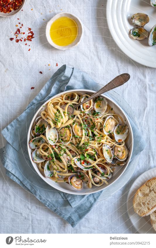 Draufsicht auf Pasta vongole, Linguini mit Venusmuscheln, roten Pfefferflocken und Olivenöl auf weißem Hintergrund mit blauer Serviette Food-Styling
