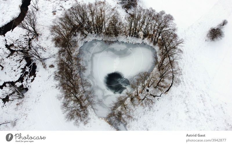 Luftaufnahme von einer Drohne von einem zugefrorenen See in Herzform oder Dreiecksform im Winter luftaufnahme drohnenfoto see gewässer eis winter schnee