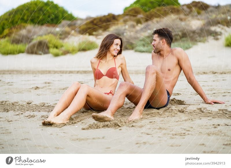 Junges Paar sitzt zusammen auf dem Sand des Strandes Frau Mann Bikini Sommer Körper Freizeit Lifestyle Mädchen Küste im Freien genießend Menschen weiß