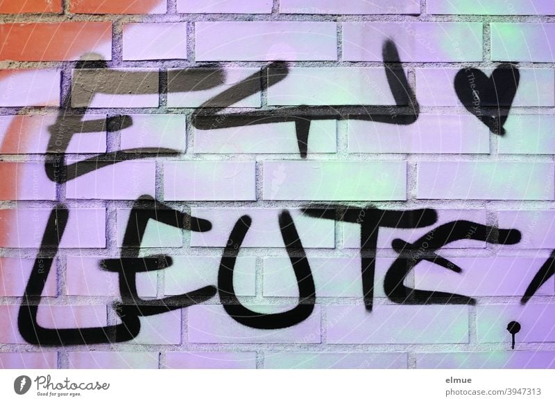 Ein kleines Herz und "EY LEUTE !" sind in schwarz auf eine grün-lila Ziegelwand gesprayt / Graffito / Jugendsprache / Lifestyle Ey Leute Graffiti sprayen