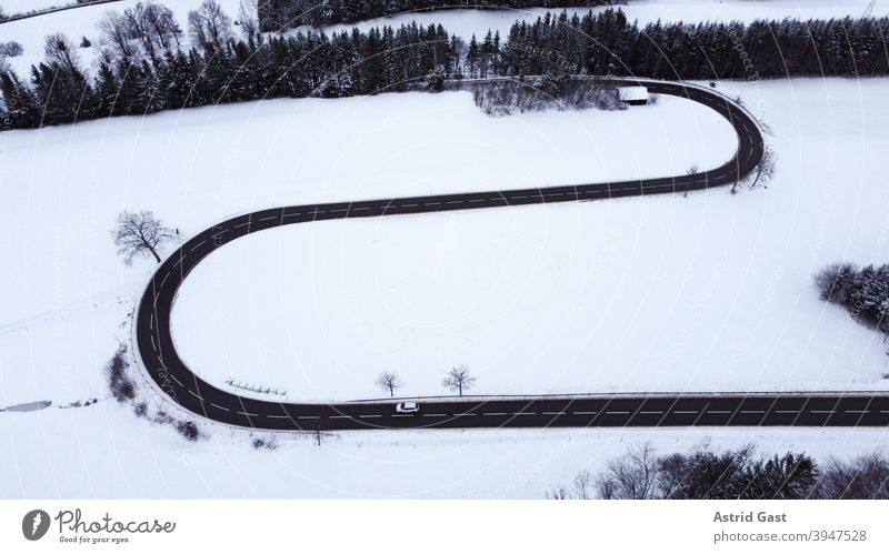 Luftaufnahme mit einer Drohne von einer Straßenkurve mit einem fahrenden Auto im Winter luftaufnahme drohnenfoto auto winter straße schnee kehre straßenkurve