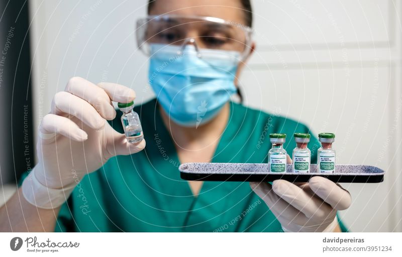 Weiblicher Labortechniker bei der Untersuchung eines Fläschchens mit Coronavirus-Impfstoff. pharmazeutisches Labor Laborantin covid-19 Untersuchen Tablett