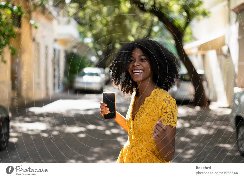 Junge schwarze Frau mit lockigem Haar, in gelbem Kleid und mit Stilen, Haltung, lachend, glücklich Individualität Ethnizität Haut Lächeln Frisur Nachricht