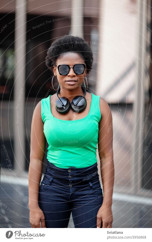 Eine junge afrikanische Frau mit Kopfhörern und Sonnenbrille lächelt fröhlich und schaut in die Kamera Afrikanisch Glück Lächeln positiv Blick Mädchen Musik