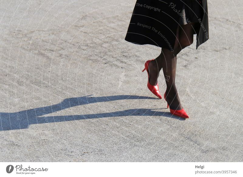 Beine einer eleganten Dame in roten Pumps und schwarzen Strümpfen sowie schwarzem Mantel mit langem Schatten auf Steinboden Frau Schuhe Licht gehen