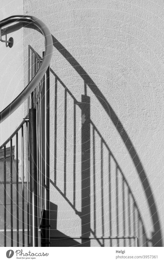 Treppengeländer mit Schattenwurf an einer Wand Geländer Licht gebogen gerade Menschenleer Außenaufnahme Gebäude schwarz weiß grau Kontrast Linien Muster