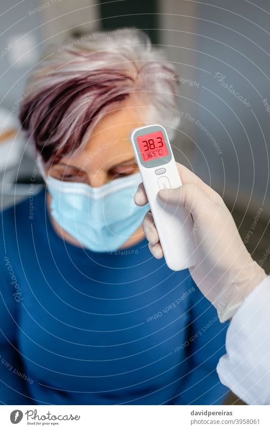 Ältere Frau mit Fieber, deren Temperatur von ihrem Arzt gemessen wird Senior berührungsloses Thermometer covid-19 Symptom Messung Schutzmaske Überprüfung