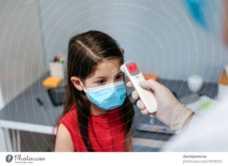 Mädchen mit Fieber, dessen Temperatur vom Arzt gemessen wird Infrarot-Thermometer Symptom Coronavirus Schutzmaske Kind covid-19 krank kalt wenig digital