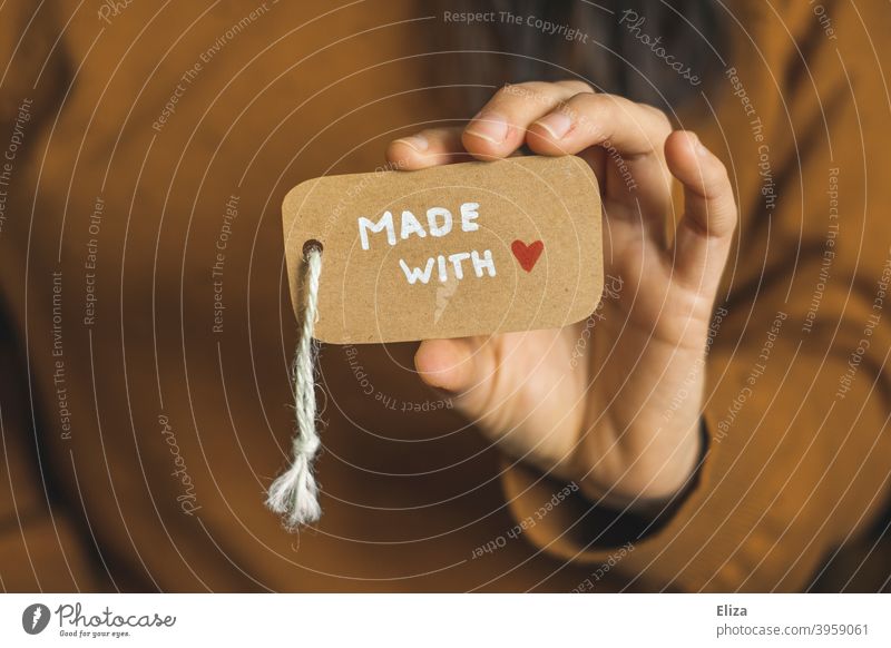 Person hält ein Etikett auf dem Made with love steht. made with love handarbeit liebevoll einkaufen Konsum lokal Kleinunternehmen selbstgemacht Schild