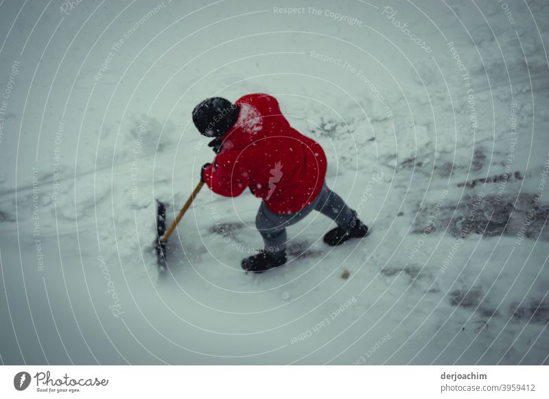 Eine Person mit roter Jacke und schwarzer Mütze , schiebt mit einer Schnee Schaufel den Schnee  mühsam und mit viel Kraft aus dem Weg. schnee räumen Winter kalt