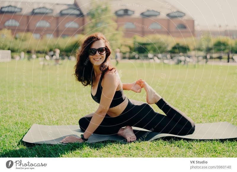 Glücklich fit junge Frau tut Stretching-Training auf Fitness-Matte Praktiken Yoga außerhalb in activewear gekleidet hat starken Körper atmet frische Luft im Freien führt aktiven Lebensstil. Sport Fitness Konzept