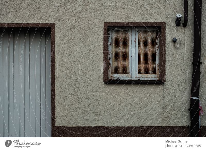 Alte Hauswand mit rostigem Gitterfenster, Wasserrohr und Garage Hauswandfenster Wand Fassade Außenaufnahme Menschenleer Mauer Gebäude Farbfoto trist Stadt
