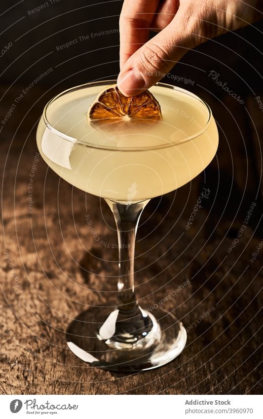 Person mit Alkoholcocktail Cocktail gelb orange Scheibe trinken hinzufügen Garnierung trocknen getrocknet Getränk Glas Schnaps geschmackvoll Tisch lecker